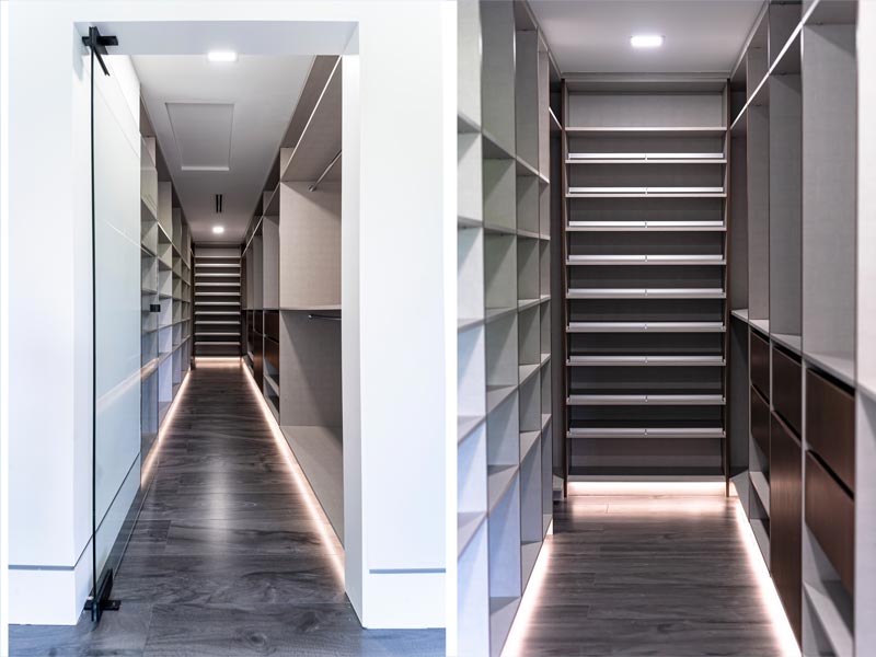 Dos vestidores angostos con estantería de piso a techo, gavetas de madera oscura e iluminación LED a nivel del piso que recorre todo el cuarto