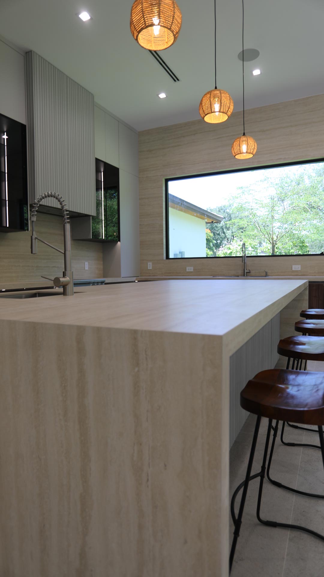 Custom travertine kitchen island with bar seating beside a servery window in a Miami home.