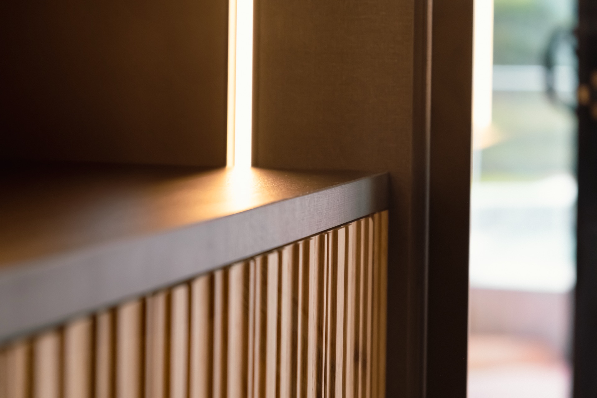 Close view of a fluted wood cabinet front meeting the squared edge of a stone counter, with a warm vertical light strip behind.