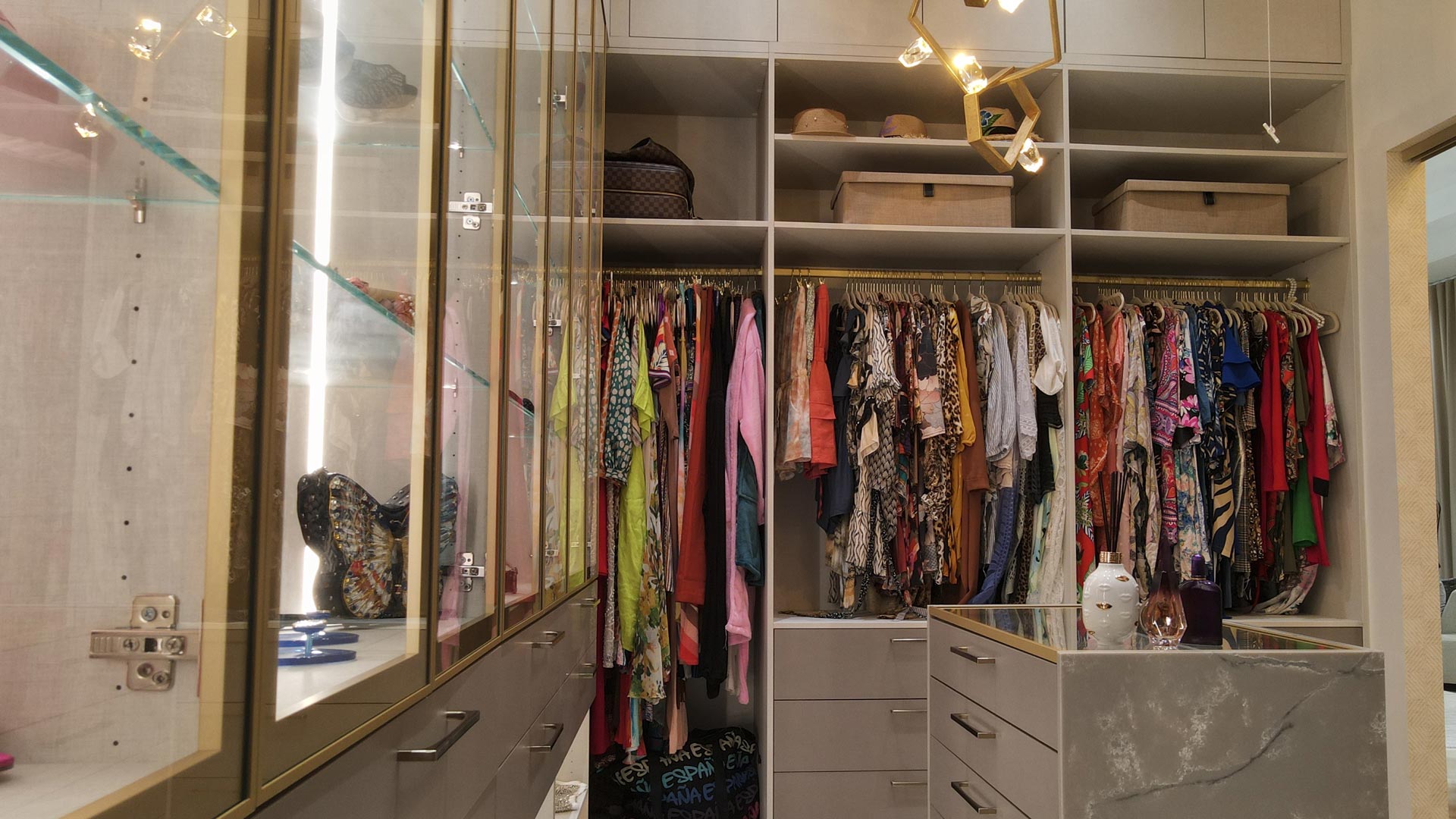 Custom walk-in closet with full-height storage, lit glass display cabinets and a stone-topped island