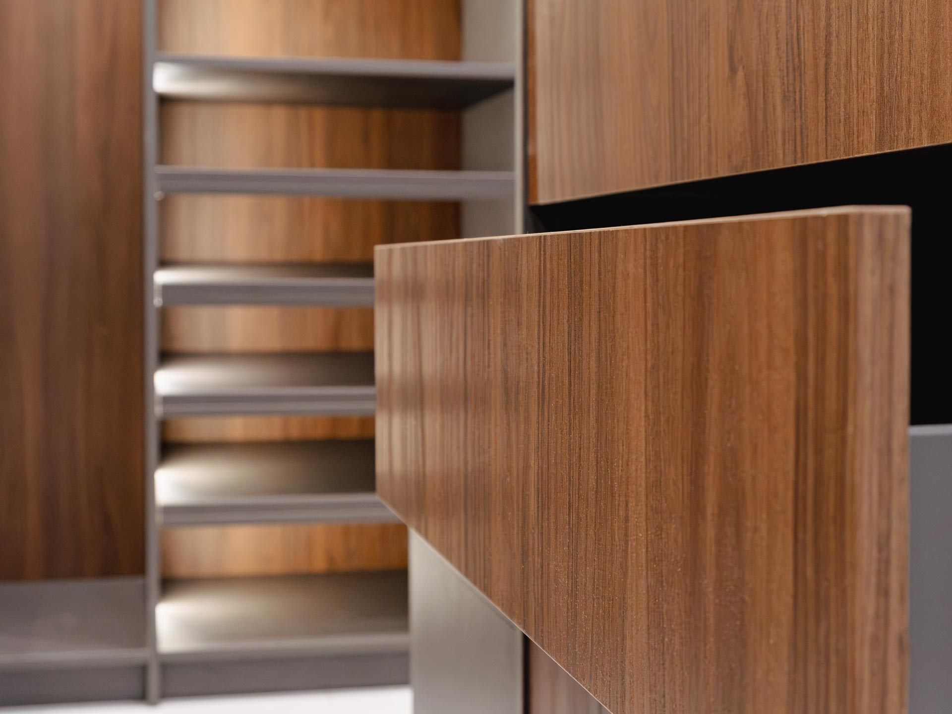 Pull-out shoe shelving beside a drawer front in a walnut closet system