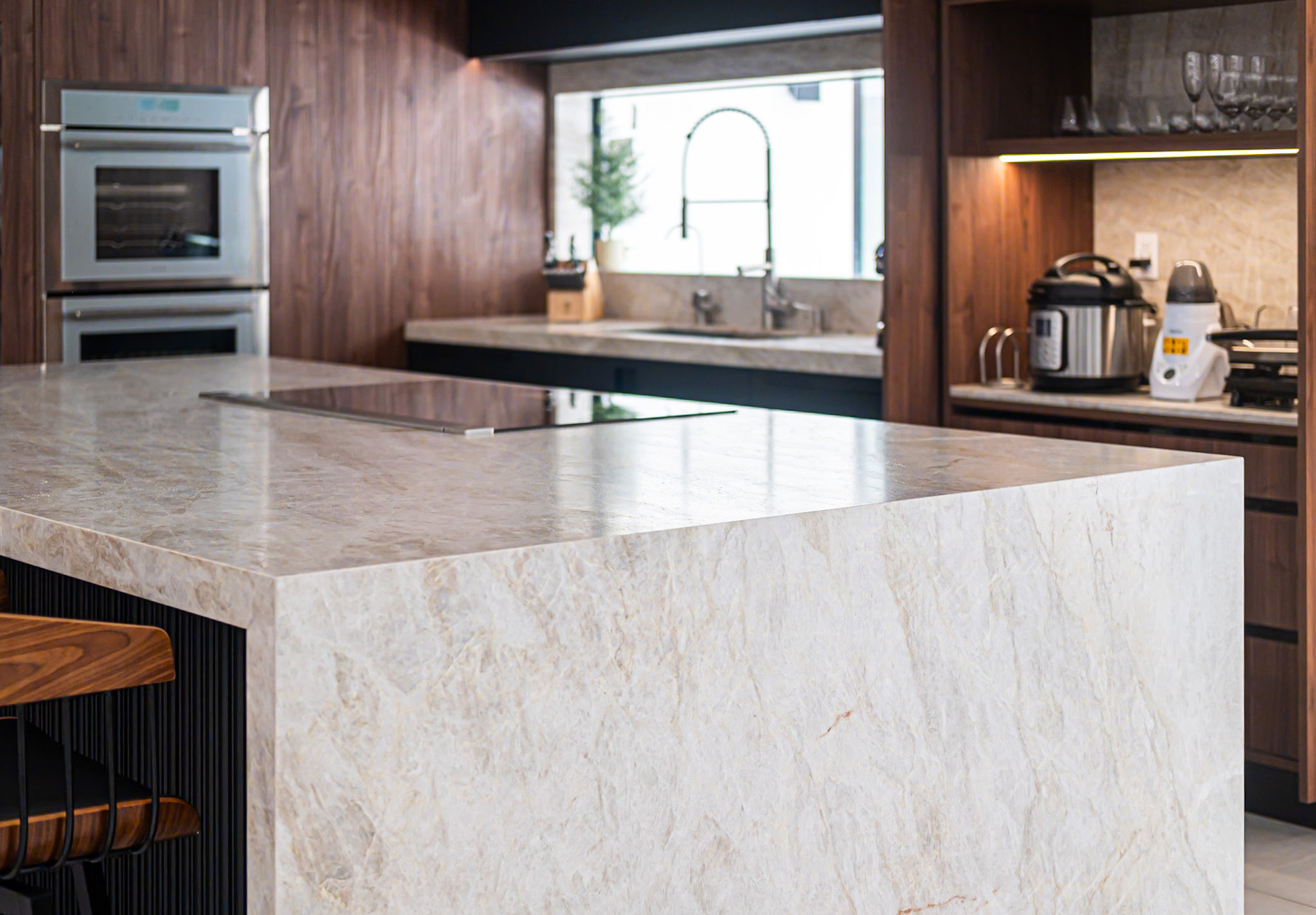 Custom kitchen in Doral with a quartzite waterfall countertop, walnut cabinetry and integrated stainless appliances.