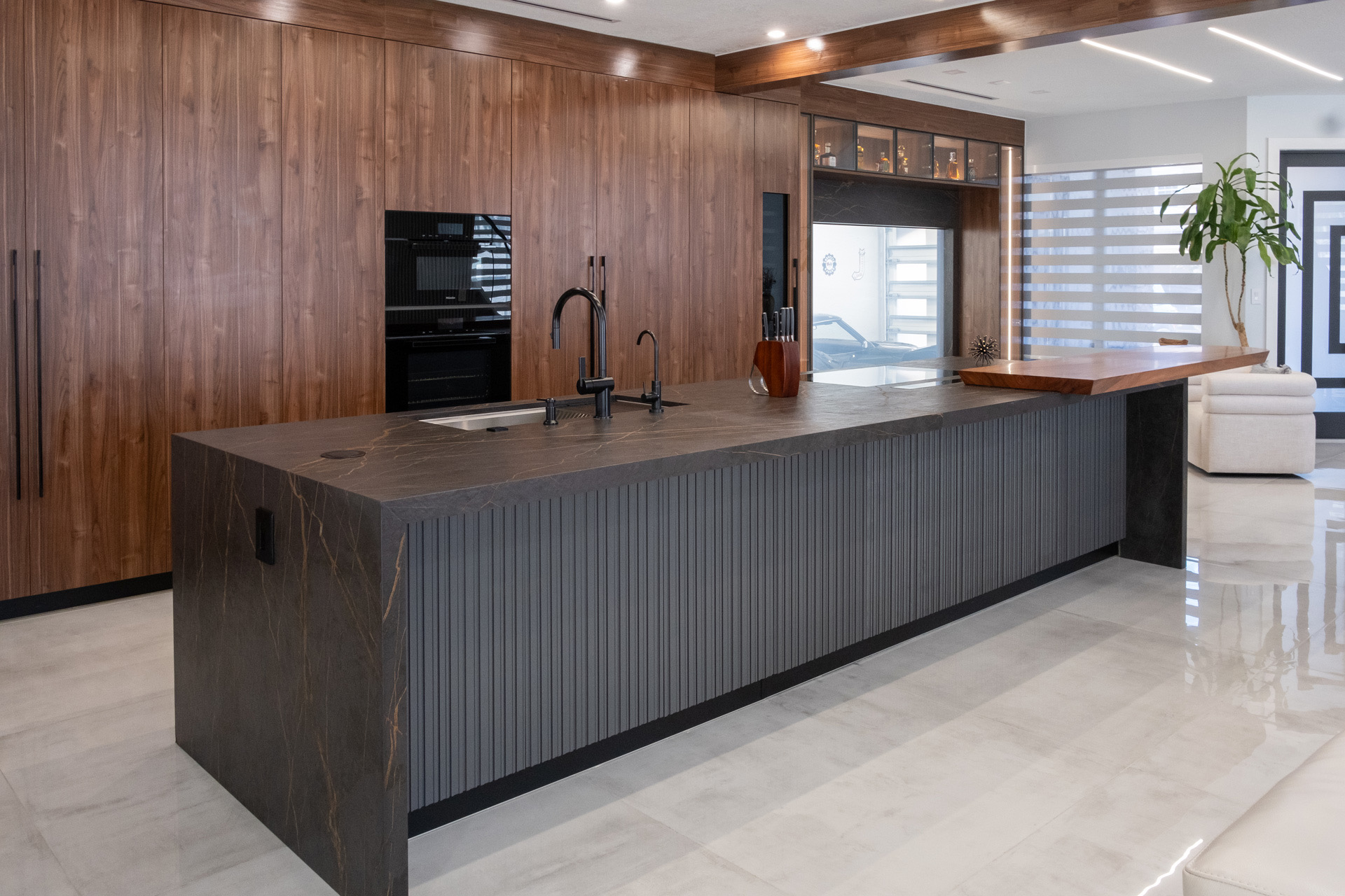 Custom Miami kitchen with full-height walnut cabinetry, a dark stone waterfall island with a fluted base and integrated black fixtures.