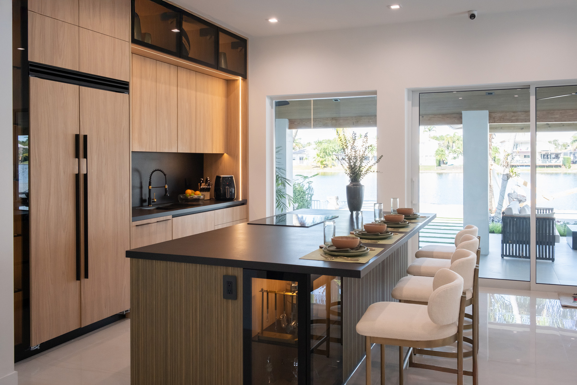 Bright custom kitchen in Miami with light oak cabinetry, a black island set for dining and a waterfront view, staged to show resale appeal.